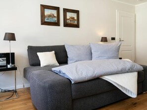 A modern bedroom with a grey sofa bed, a flat-screen TV, and two framed pictures on the wall. - Holiday Apartment With 1 Bedroom (Sylt)
