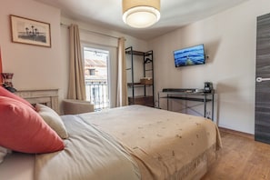 A bedroom with a bed, a desk, a television, and a window with curtains.
