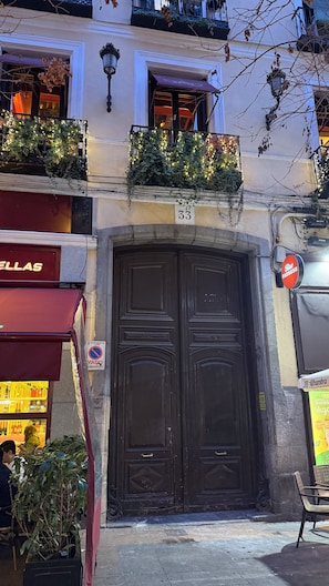 A building with a dark wooden double door, a balcony with plants and lights, and a sign with the number 33.