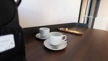 A wooden table with two white cups and saucers, a tray with a teapot and sugar cubes, and a door in the background.