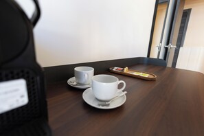 Una mesa de madera con dos tazas y platillos blancos, una bandeja con tetera y terrones de azúcar, y una puerta al fondo.
