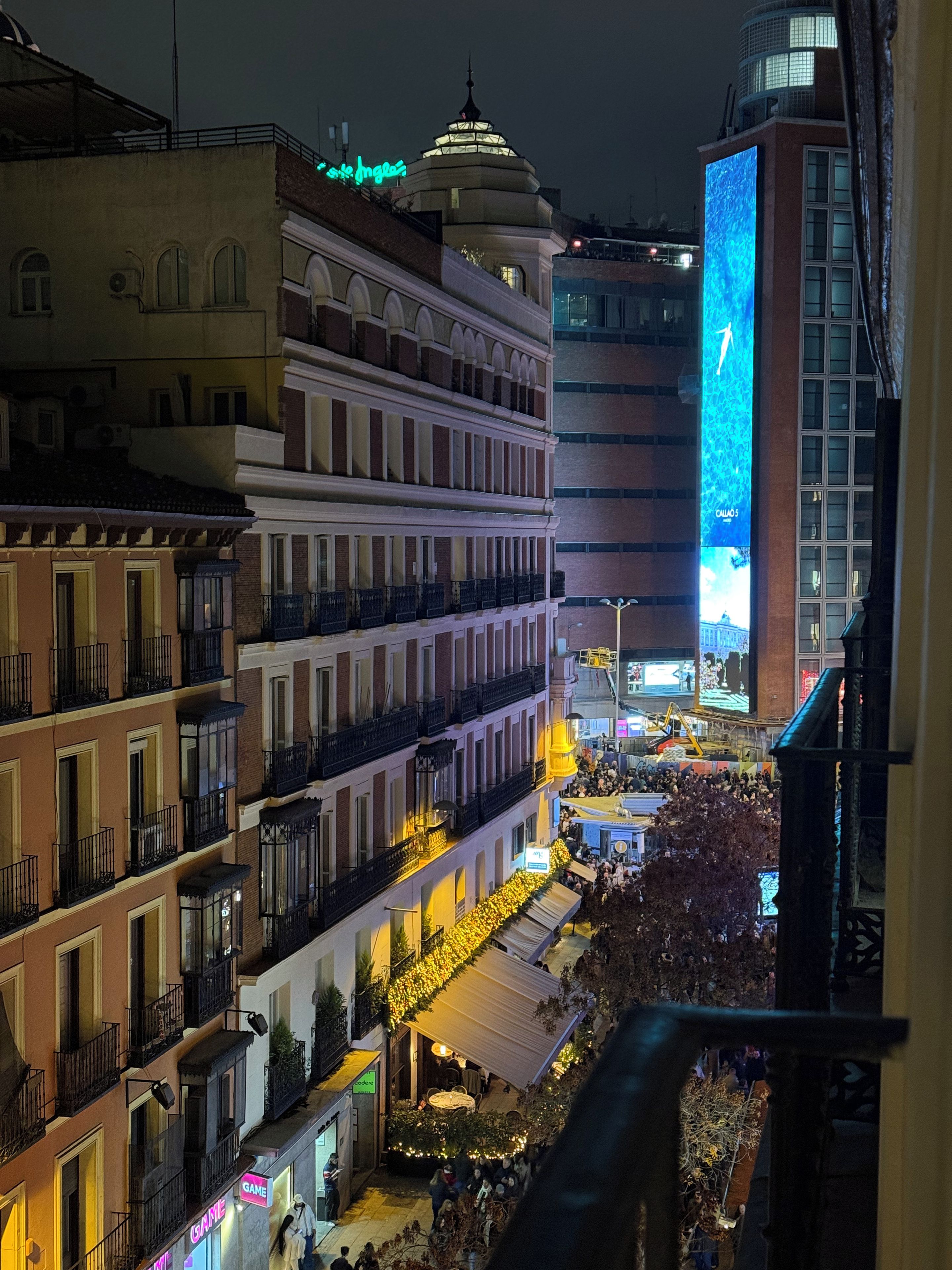 Un paisaje urbano nocturno con edificios, una pantalla iluminada grande y una multitud.