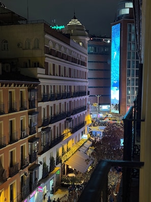 Un paisaje urbano nocturno con edificios, una pantalla iluminada grande y una multitud.