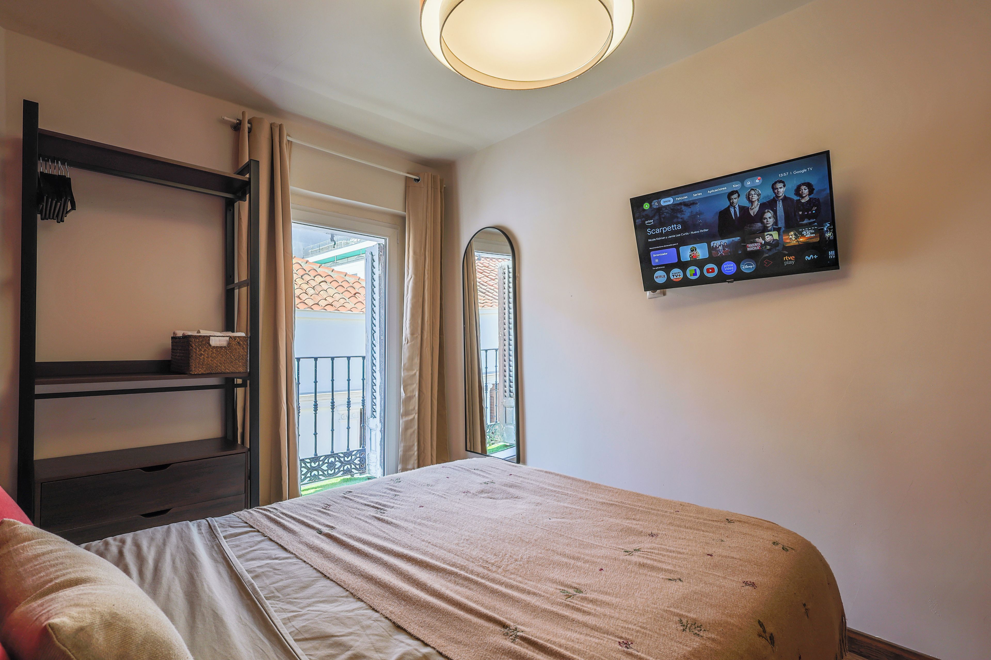 A hotel room with a bed, a TV mounted on the wall, a window with curtains, and a balcony.