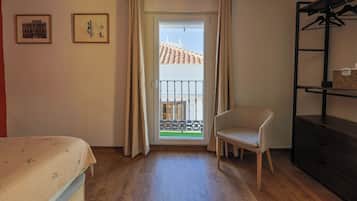A room with a bed, a chair, a balcony with a railing, and two framed pictures on the wall.
