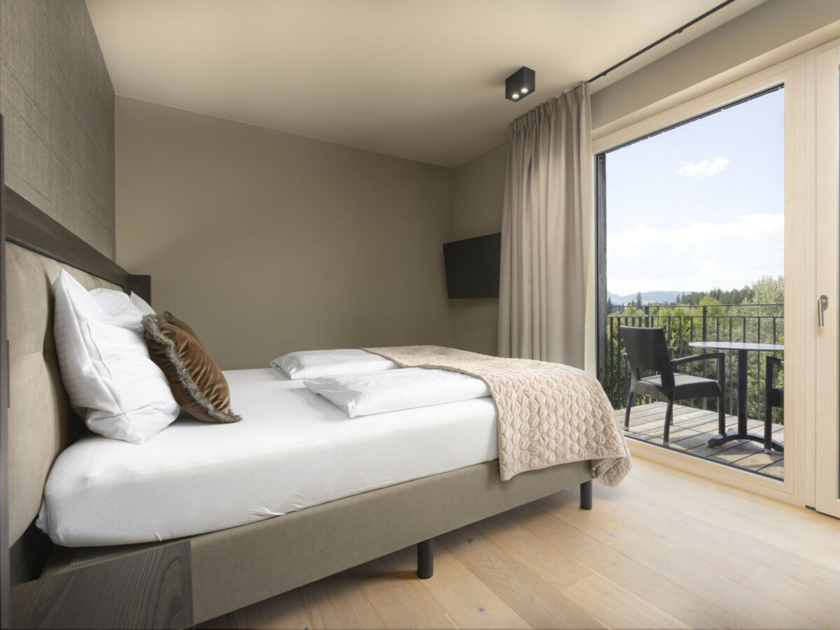 A modern bedroom with a large bed, a television, and a balcony with a table and chairs.