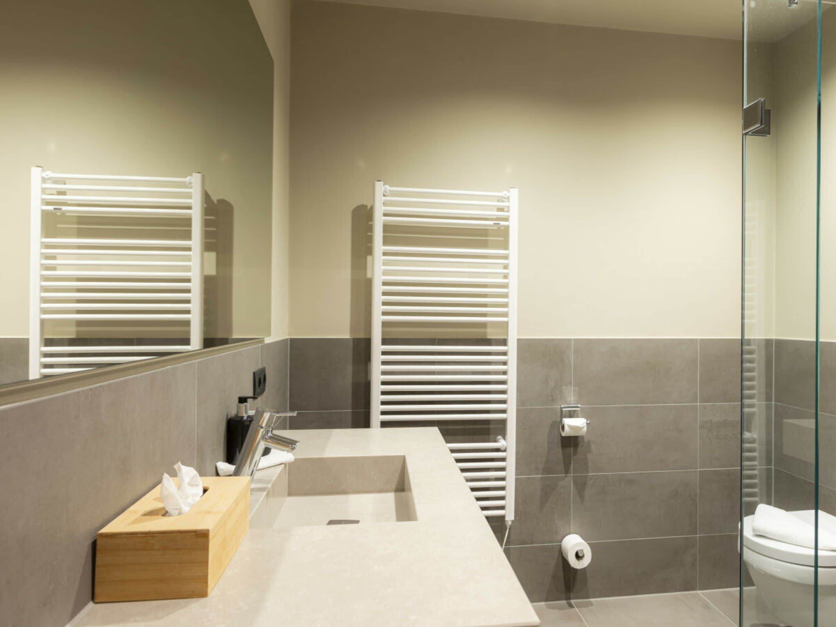 Une salle de bain moderne avec un lavabo rectangulaire, un porte-mouchoirs en bois, un porte-serviettes et une paroi de douche en verre.