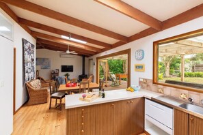 A kitchen with wooden beams, a dining area with wicker furniture, and a view of the outdoors.