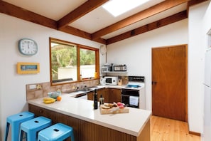 A kitchen with a central island, wooden beams, a clock, and a window.