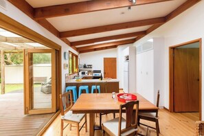 A dining area with a wooden table and chairs, a kitchen in the background, and a sliding glass door leading to an outdoor deck.
