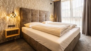 Quarto de hotel com uma cama grande, mesa de cabeceira, luminária na parede e janela com cortinas.