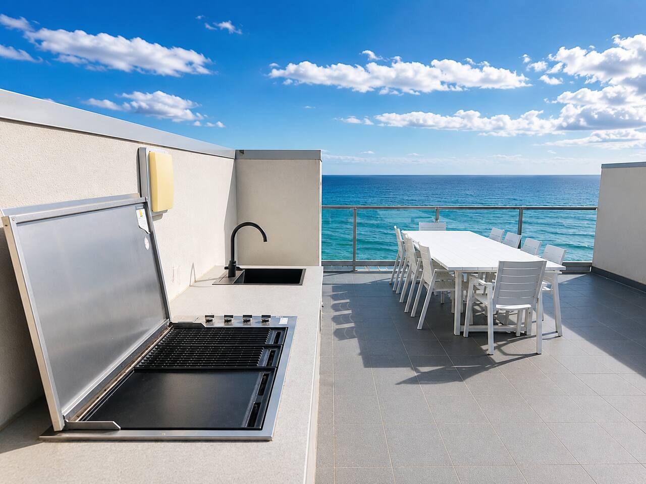 Eine Dachterrasse mit Grill, Esstisch und Stühlen, mit Blick auf das Meer.