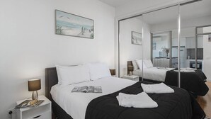 Una habitación de hotel moderna con una cama grande, una mesita de noche con lámpara, una revista y un cuadro en la pared.