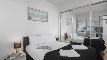 A modern hotel room with a large bed, a bedside table with a lamp, a magazine, and a painting on the wall.