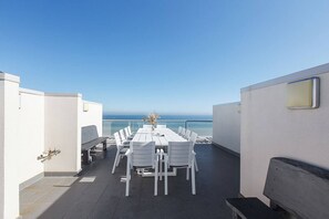 A rooftop terrace with a long dining table and chairs, a small seating area, and a view of the ocean. - Bonbeach Bliss Contemporary Waterfront Living (Bonbeach)