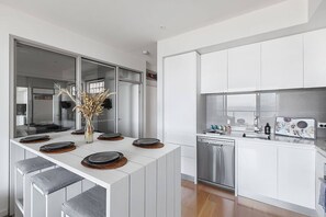 Una cocina moderna con muebles blancos, una isla central con taburetes y un lavavajillas empotrado.