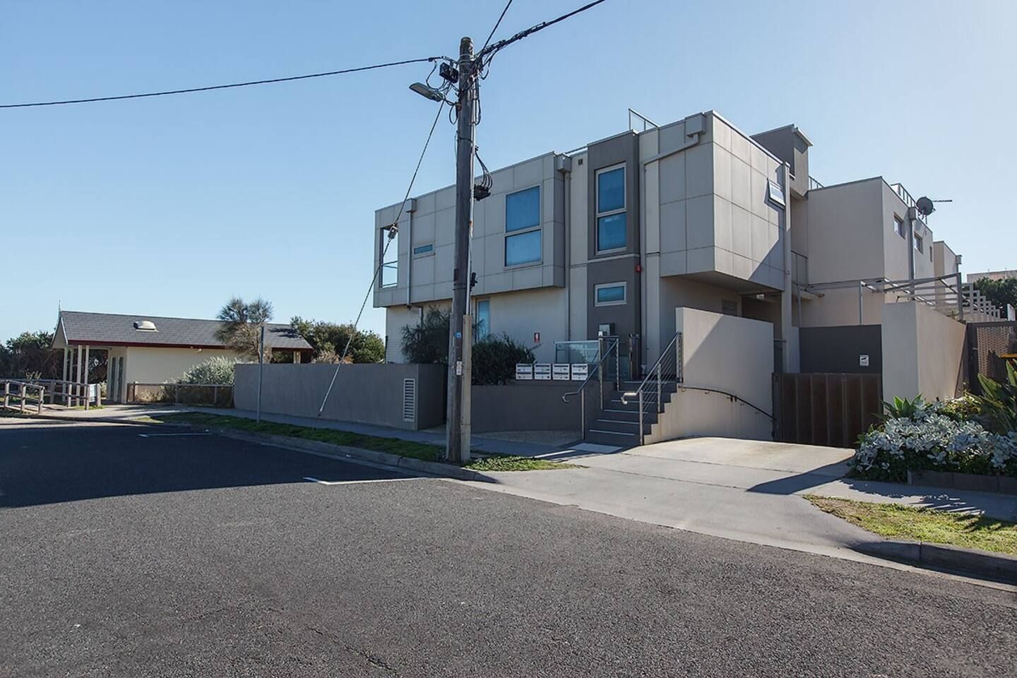 A modern two-story building with a flat roof, a staircase leading to the upper floor, and a small garden area in front.