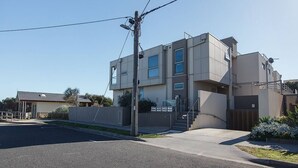 Un moderno edificio de dos pisos con techo plano, una escalera que conduce al nivel superior y un pequeño jardín frontal.