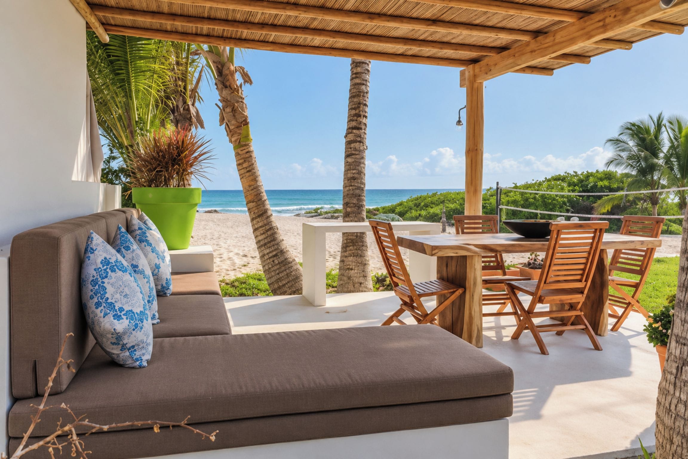 Un espace extérieur aménagé, abrité et doté d’un canapé, de chaises et d’une table, offrant une vue sur une plage bordée de palmiers et sur l’océan.