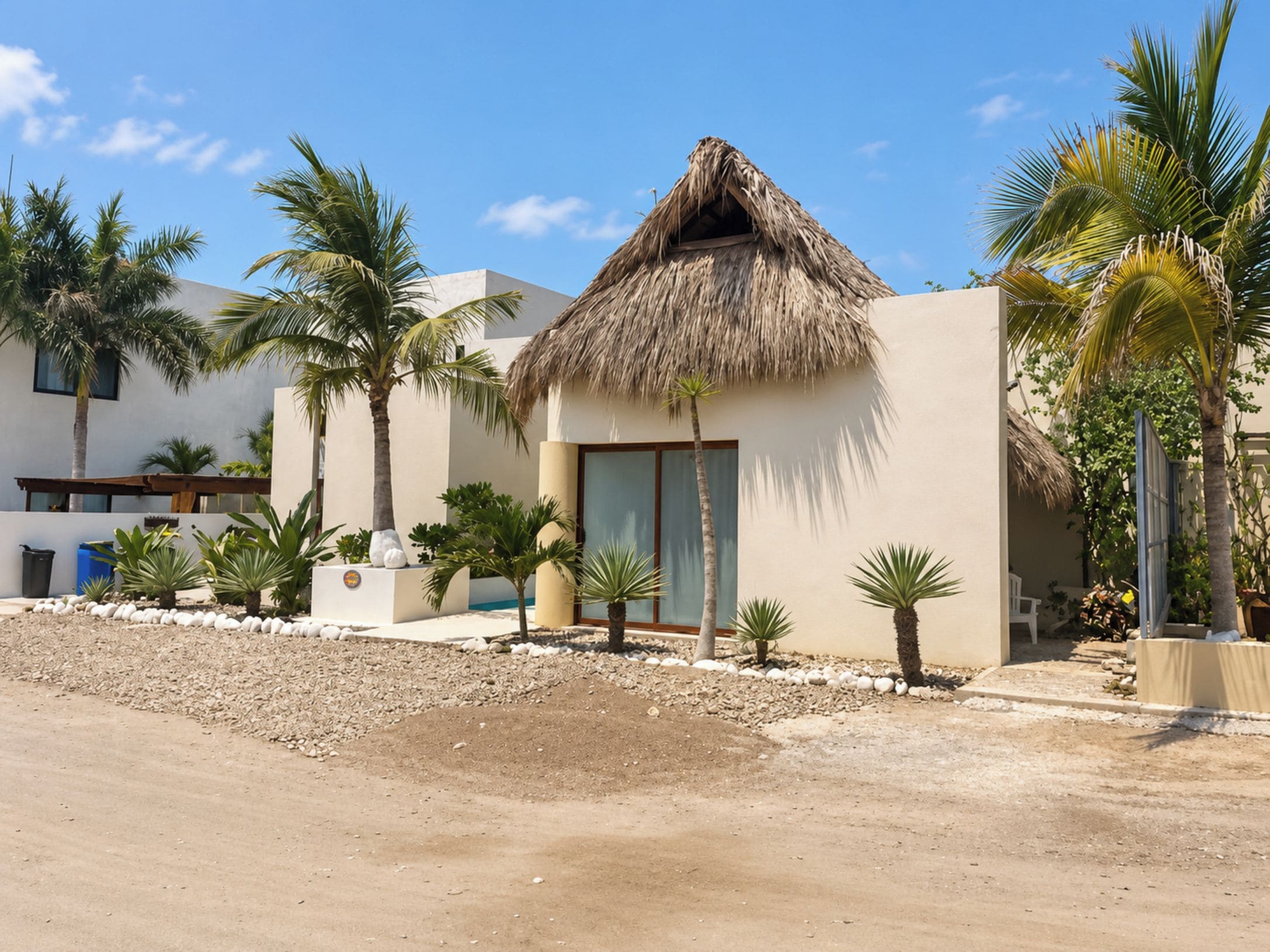 Un resort con una cabaña de techo de paja, palmeras y un paisaje arenoso.