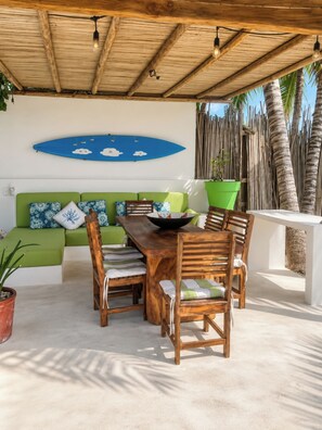 An outdoor seating area with a wooden table and chairs, a green sofa, and a blue decorative wall piece. - Casa Serena (Santa María Colotepec)