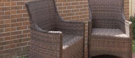 Two wicker chairs outside a brick wall with a bird decoration.