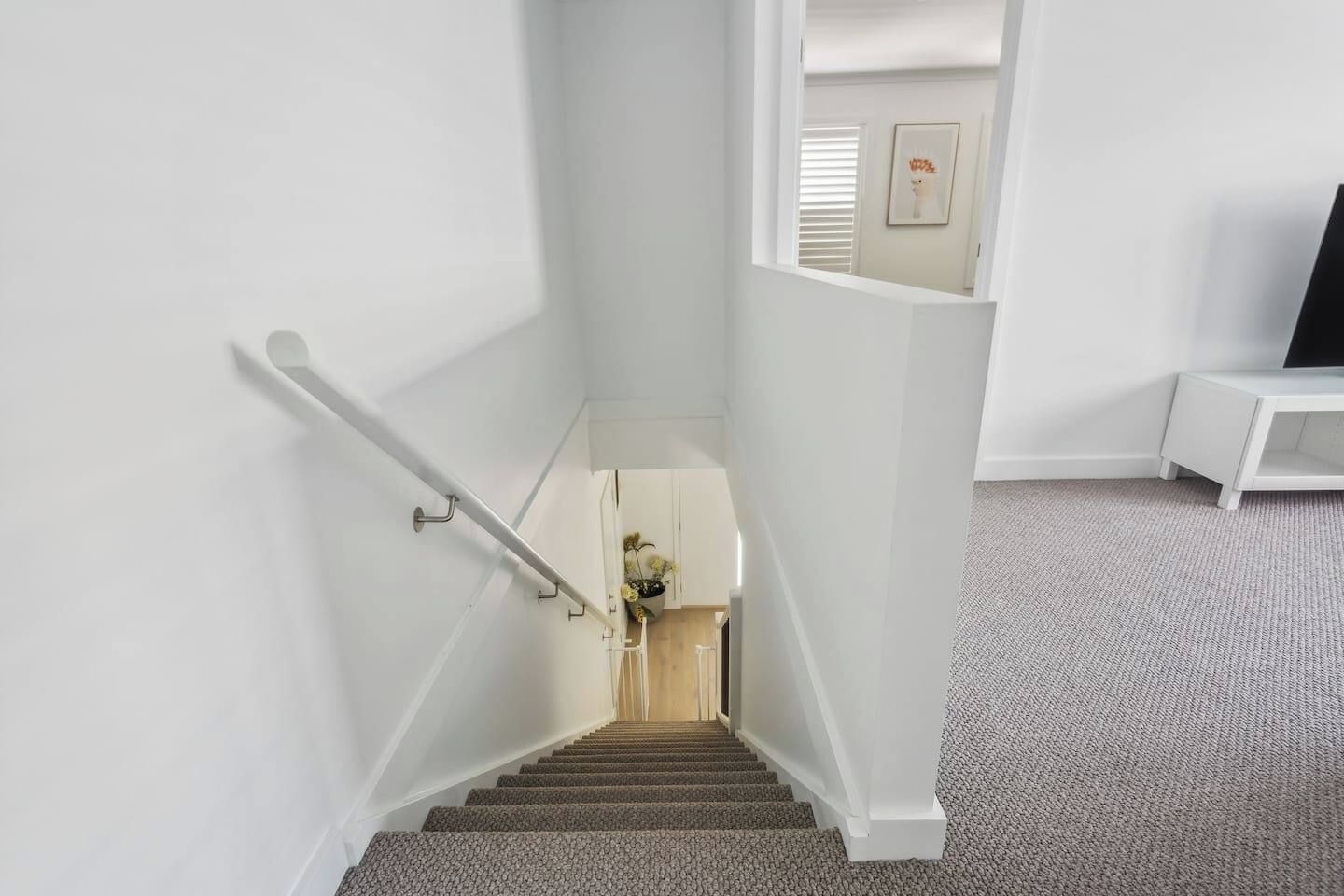Een trap met een leuning, bekleed met tapijt, en een witte muur.