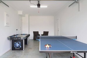 A ping pong table with a net, a billiards table, and two chairs in a room with white walls and a ceiling-mounted projector. - Hamptons Style Haven for Laidback Family Living (Rosebud)