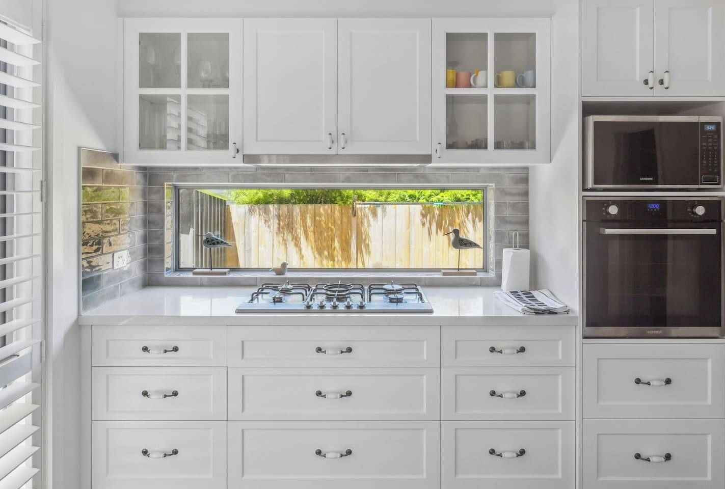 Une cuisine moderne avec des meubles blancs, une cuisinière à gaz, un four à micro-ondes et une fenêtre donnant sur un paysage verdoyant.