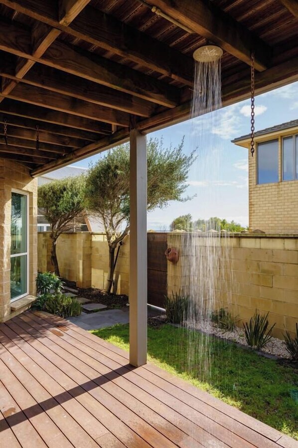 A covered outdoor area with a wooden deck, a hanging water feature, and a brick wall.