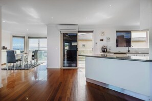 Una cuina moderna amb una illa gran, una zona de menjador amb vistes i una porta corredissa de vidre que dona a un balcó.