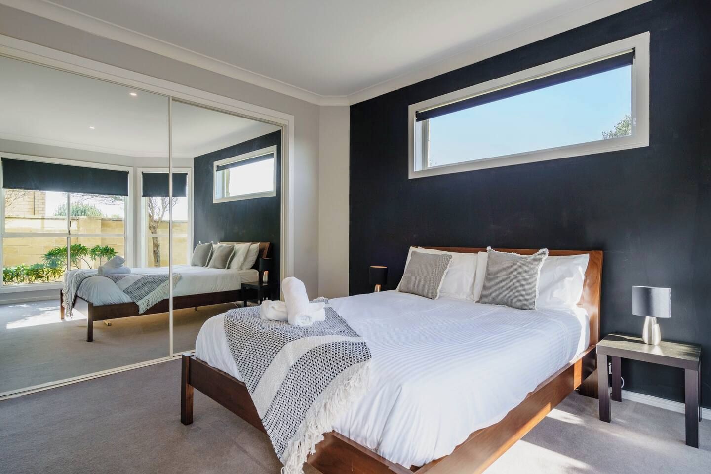 A modern bedroom with a large bed, a nightstand, a mirror, and a window.