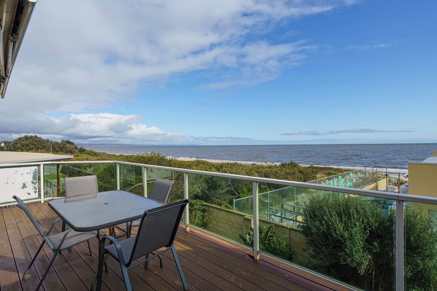 A balcony with a table and chairs, overlooking a beach and the sea.