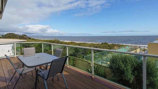 En balkon med et bord og stole, der giver udsigt over en strand og havet.