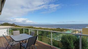 A balcony with a table and chairs, overlooking a beach and the sea.