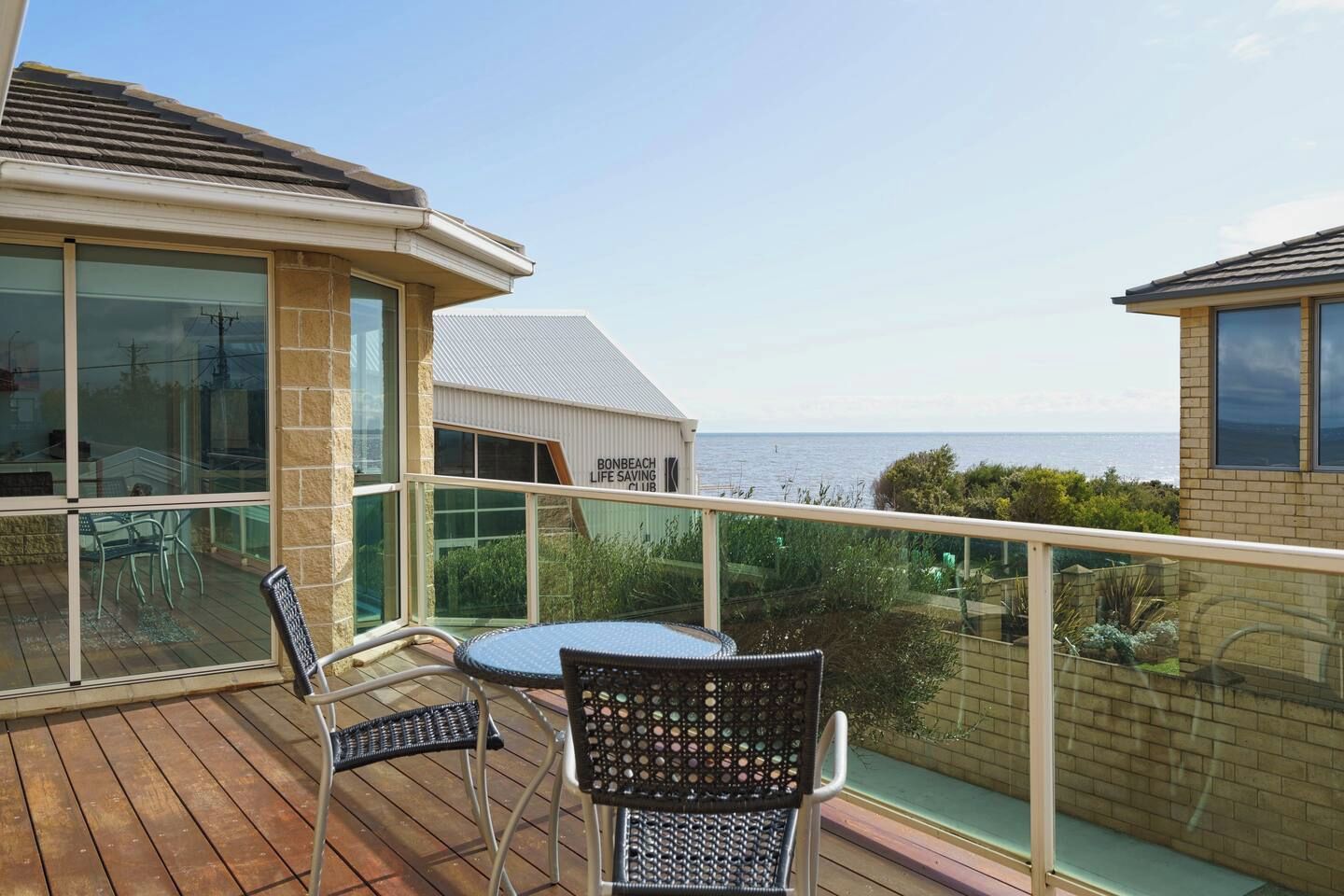 A balcony with a table and chairs, overlooking the sea.