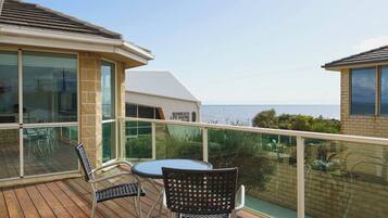 A balcony with a table and chairs, overlooking the sea.