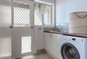A compact laundry room with a washing machine, a sink, and a window with a mesh screen.