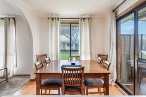 A dining room with a large wooden table, six chairs, and a view through a glass door to the outside. - Solanders Retro Residence Calming Days by the Sea (Dromana)