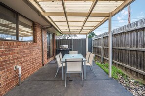 Een overdekte patio met een tafel, stoelen, een barbecue en een bakstenen muur.