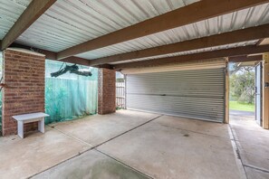 A covered outdoor area with a concrete floor, a closed metal garage door, and a brick wall with a bench. - Solanders Retro Residence Calming Days by the Sea (Dromana)