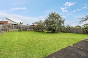 A backyard with a wooden fence, a lawn, and a tree. - Solanders Retro Residence Calming Days by the Sea (Dromana)