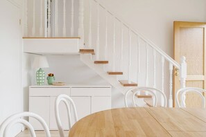A dining area with a wooden table and chairs, a white staircase with wooden steps, and a white door. - Hamptons on Heales Classic Beach House Charm (Dromana)