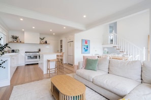 A modern kitchen with white cabinetry, a central island, and a dining area with white chairs. - Hamptons on Heales Classic Beach House Charm (Dromana)