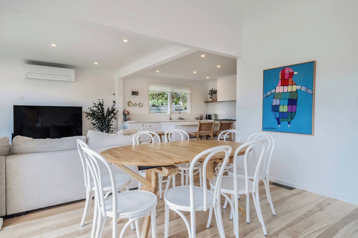 Un salon moderne avec une table à manger en bois entourée de chaises blanches, un canapé et un téléviseur à écran plat.