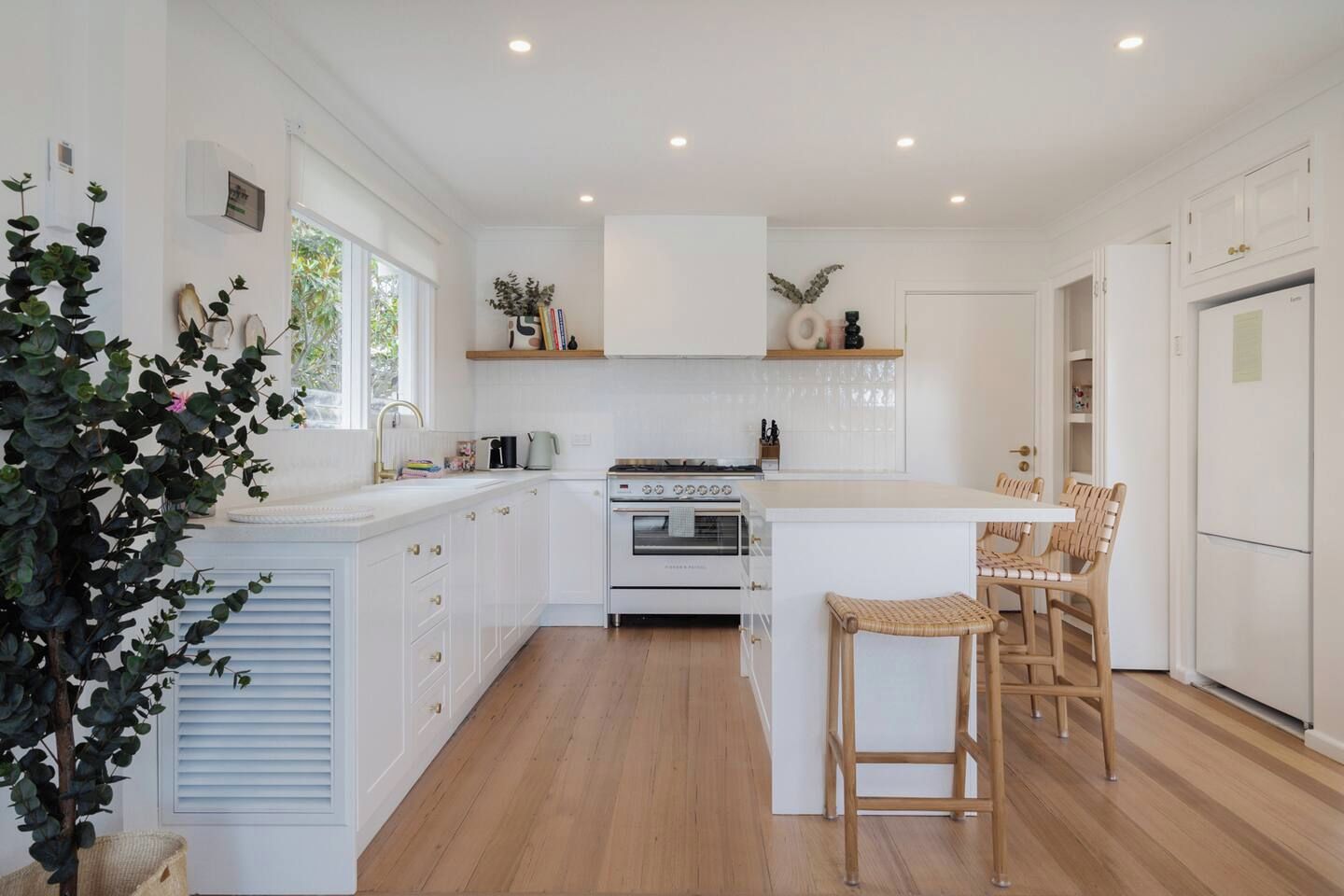 A modern kitchen with white cabinetry, a central island with bar stools, and a built-in oven.