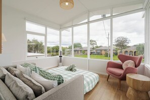 A cozy room with a large window, a bed, a chair, and a small table. - Hamptons on Heales Classic Beach House Charm (Dromana)