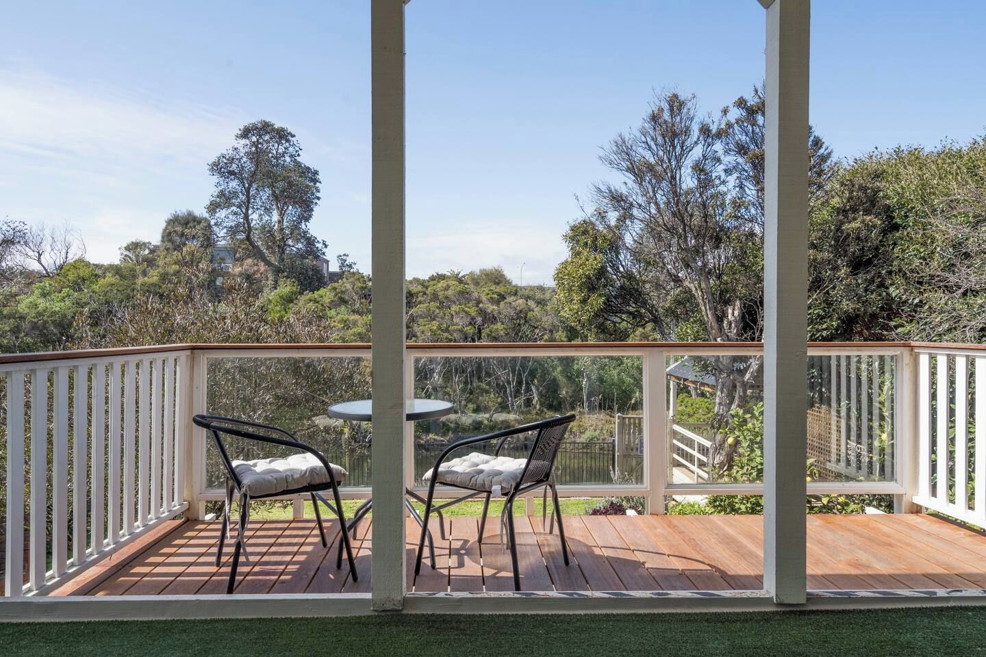 A covered outdoor area with two tables and chairs, surrounded by a white railing, overlooking a natural landscape.