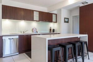 Una cuina moderna amb rentaplats integrat, una illa gran amb tamborets i armaris de fusta.