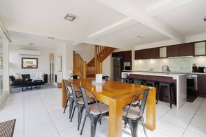 A modern kitchen with dark wooden cabinets, a central island, and a built-in oven. - Willow Landing Beach House with Private Jetty (Frankston)